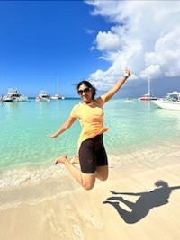 Divya in midair after jumping on a sandy beach.